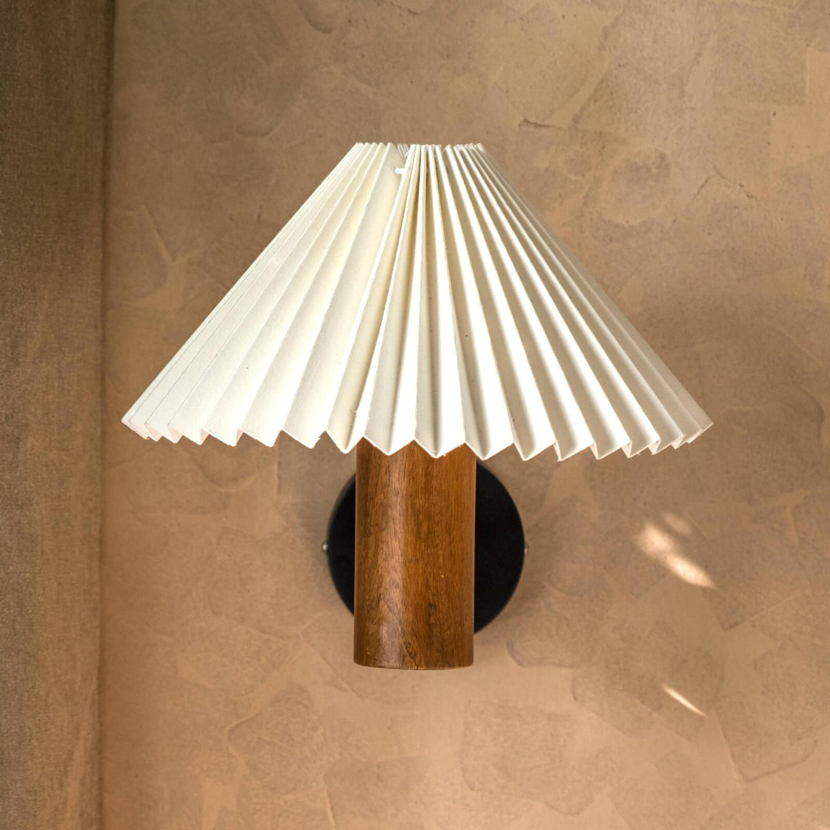 White pleated shade wall lamp with a natural wooden cylindrical base in walnut finish, perfect as a bedside wall lamp or decorative wall sconce for minimalist and vintage interiors.